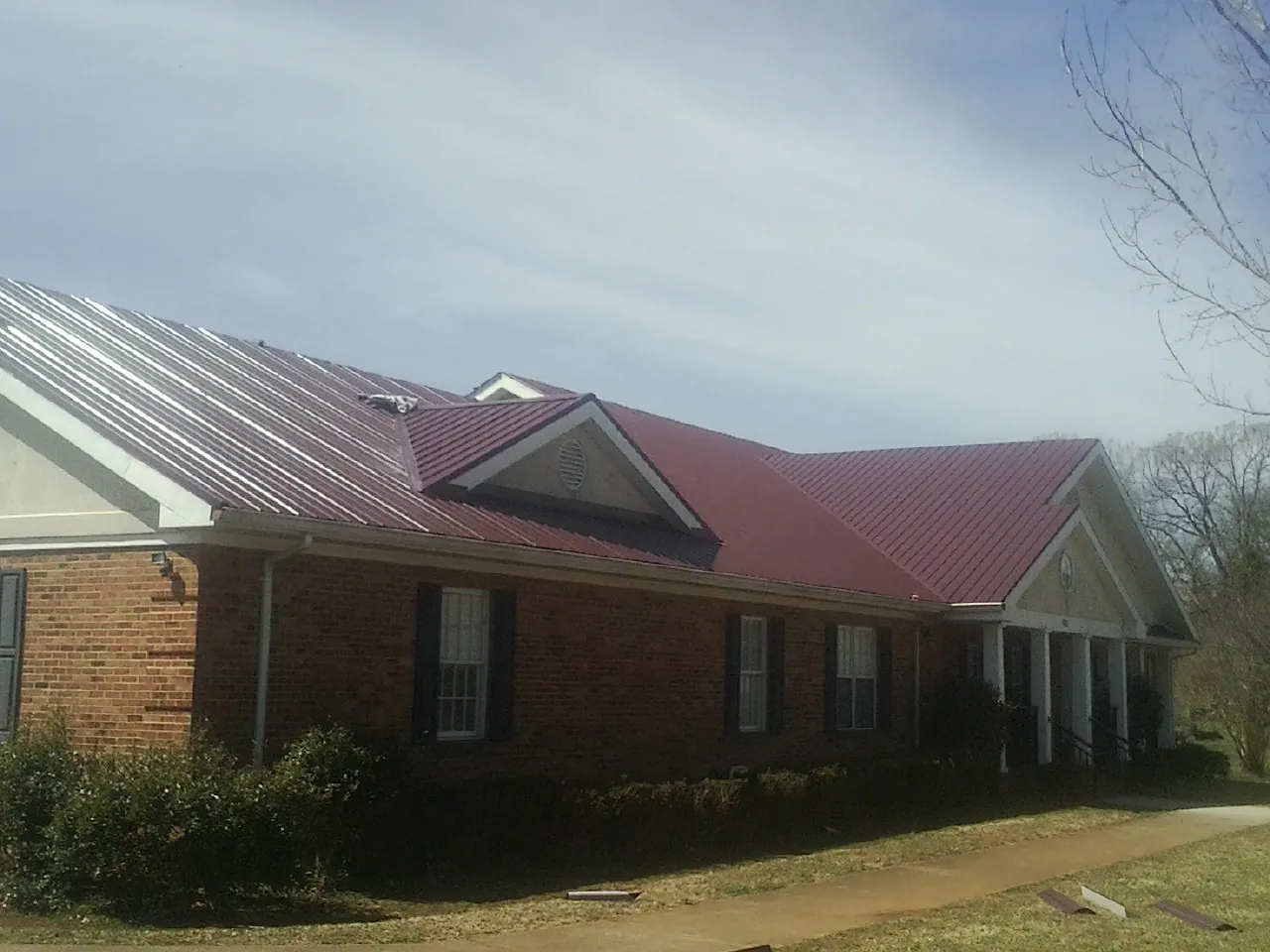 Red metal roof with gabled entries on a long brick building, from a Hail Damage Roof Repair job in Aromas