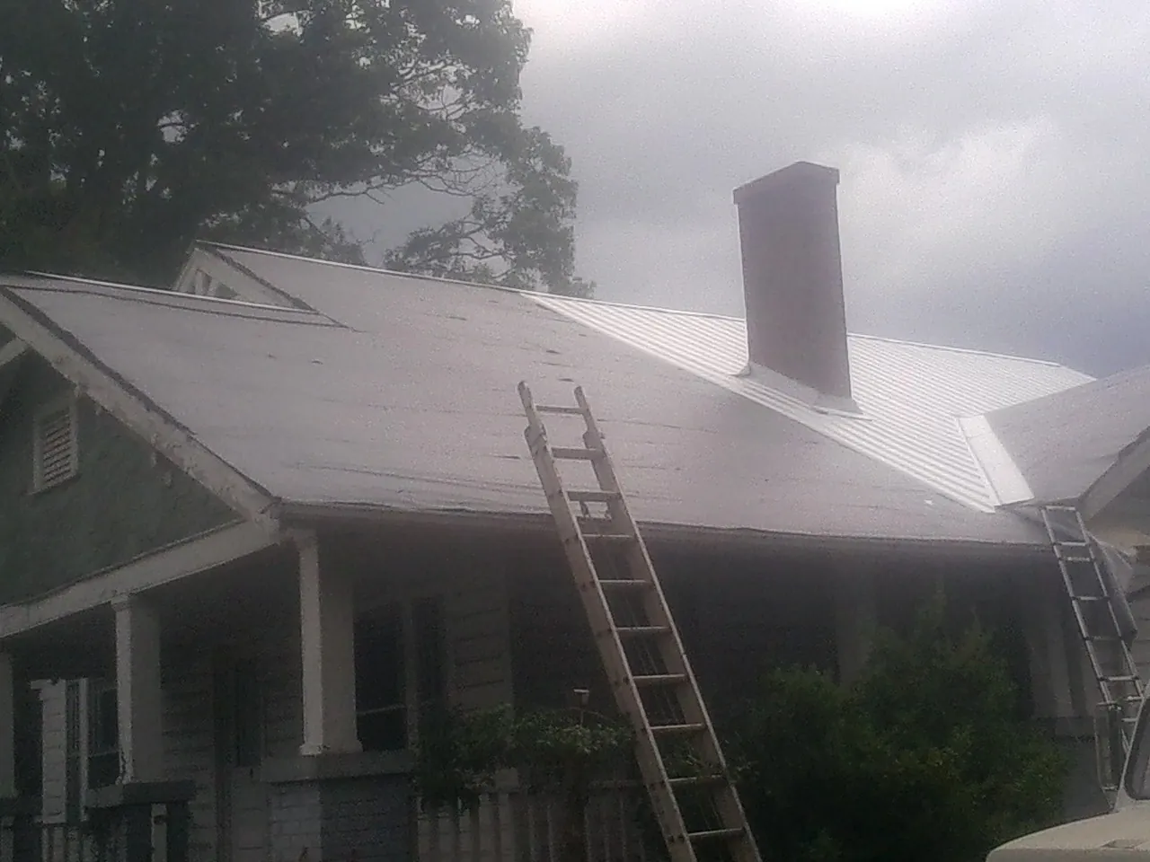 Ladders against a metal roof on an older home with a brick chimney in Aromas